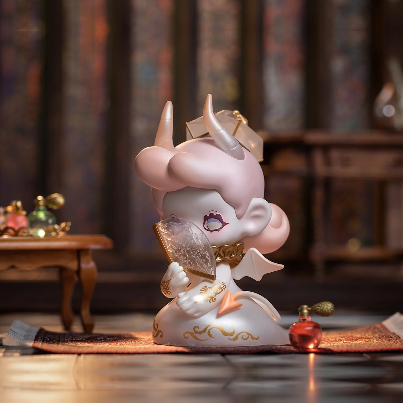 A small figurine from the Lucky EMMA - Killa Treasure Pavilion Blind Box, complete with horns and wings, rests on a carpet while holding a large crystal like a hidden gem. The room features a table and small decorative bottles in the background, reminiscent of whispers of secret treasures from Lucky Emma.