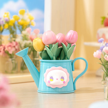 Blue watering can planter with pink and yellow tulip flowers and whimsical face decoration on wooden table