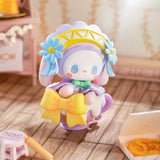 A charming figurine from the "Lucky EMMA - Secret Forest Birthday Party Blind Box" by Lucky Emma, featuring a white character adorned with blue flowers and a yellow bow, sits on a wooden floor, making it an ideal addition to your Secret Forest Birthday Party decor.