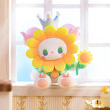 A delightful, hand-painted toy figure from the Lucky Emma brand's Secret Forest Birthday Party Blind Box collection—featuring a flower motif and crowned while holding a small sunflower—graces the windowsill as sunlight pours in, capturing an enchanting atmosphere.