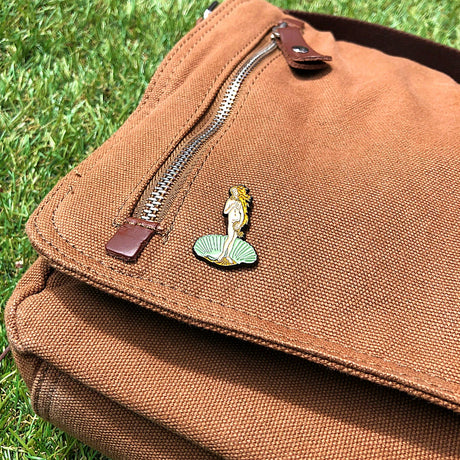 Enamel pin on tan fabric pouch, Venus on green seashell enamel design
