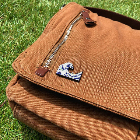 Close-up of Hokusai Great Wave enamel pin attached to brown canvas bag flap outdoors, gallery image 1 file 2.webp