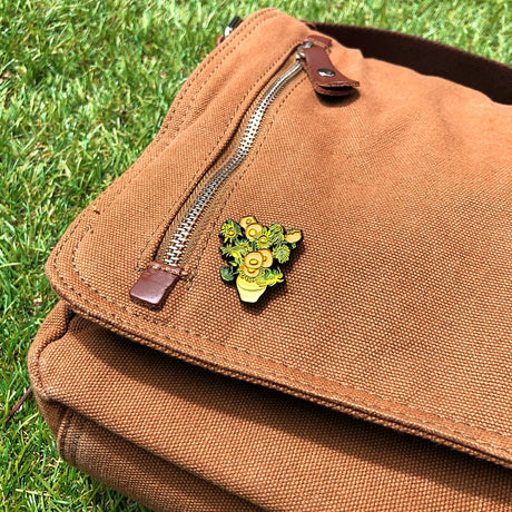 Enamel pin of Vincent van Gogh Sunflowers attached to brown canvas bag flap outdoors on grass, gallery image 1 file 5.webp