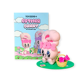 Pink Esther Bunny figure with large bow and flower basket on green base beside colorful illustrated packaging box