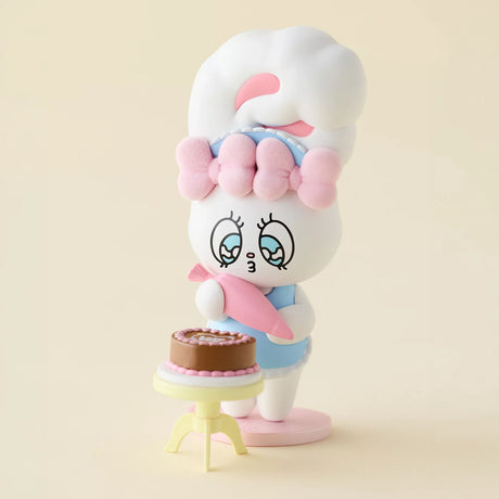 White bunny figurine wearing blue outfit, sitting by tiered cake on small stand