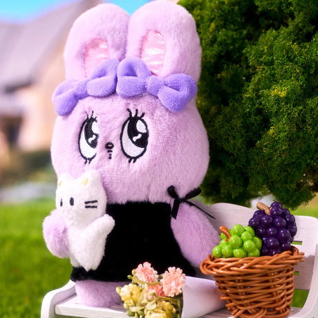 Purple Esther Bunny plush with double bows wearing black dress sitting on white bench next to basket of grapes outdoors