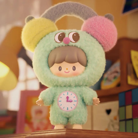 Plush keychain figure in a fuzzy green suit with colorful ears and a clock design, standing on a wooden surface indoors