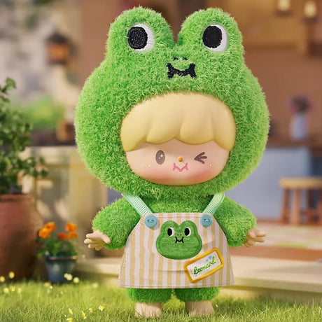 Collectible plush figure in a fluffy green frog costume with a striped apron and playful wink indoors