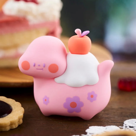 Pink Food Dinosaur Fuji Yama Vol. 2 blind box figure with white frosting and small orange fruit on wooden surface
