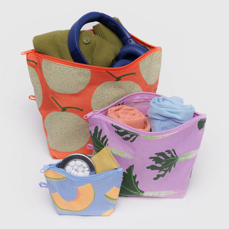 The Baggu Go Pouch Set - Japanese Produce, by Baggu, includes three zipper bags made from recycled materials. The largest fits a green sweater and blue headphones, the middle keeps rolled clothes organized, and the smallest holds a compact item with white pills for efficient organization.