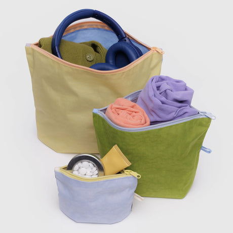 The Baggu Go Pouch Set - Pastels by Baggu includes three pouches made from recycled materials, ideal for organizing items like headphones, a sweater, rolled clothes, and toiletries such as pills and a tube.