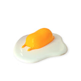 A squishy silicone Gudetama egg yolk figure lounges on a white base, illuminated by the Gudetama 3D Squishy Silicone Night Light against a stark white background.