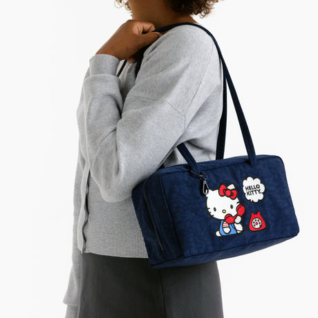 Model wearing navy Hello Kitty x Baggu nylon bowler bag with Hello Kitty graphic and shoulder straps, promo image 1