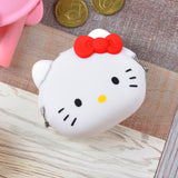 The Hello Kitty Purse Clutch by Hello Kitty, featuring a red bow, rests on a wooden surface, radiating adorable kawaii charm. Coins are scattered nearby.