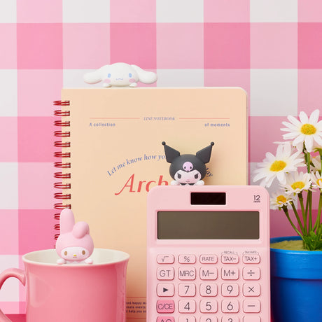 Pink calculator with black character topper, pink notebook, pink cup holding pink character toy, and white flower bouquet on pink checkered background