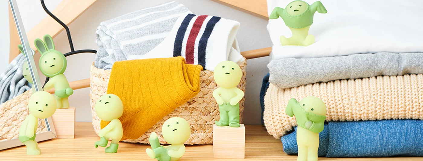 A collection of small green figurines posed around folded clothes in a basket, set on a wooden shelf.