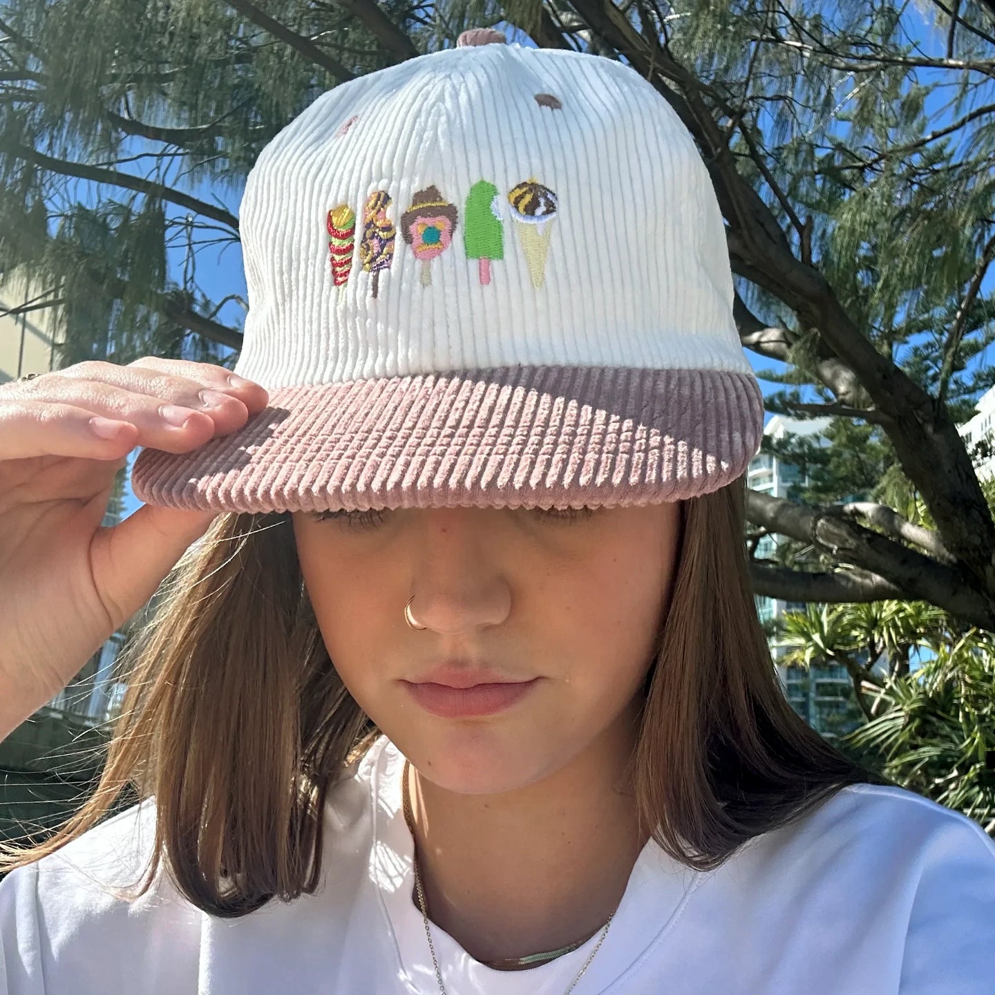 White ribbed knit hat with mauve brim and colorful character embroidery, worn facing forward