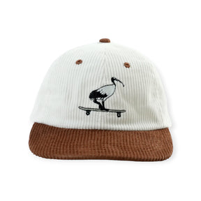 Cream corduroy cap with brown brim embroidered with black and white ibis riding skateboard on front panel