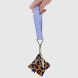 A hand holds a purple lanyard with a Baggu Logo Keychain in French Blue, clipped to a leopard-print pouch and a single key, creating an eye-catching accessory with elegance.