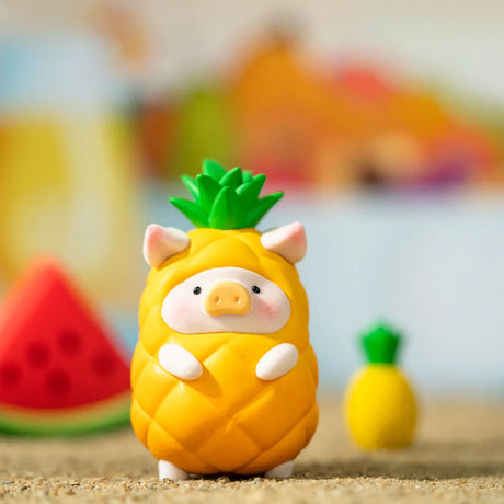 LuLu the Piggy figurine dressed as a pineapple standing on sandy surface with blurred watermelon and pineapple props
