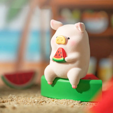 LuLu the Piggy figurine holding a watermelon slice while sitting on a watermelon block on sandy surface