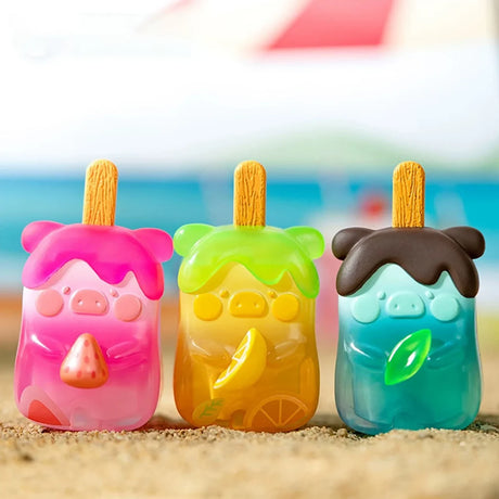Three colorful LuLu the Piggy figurines shaped like popsicles with fruit details on sandy surface