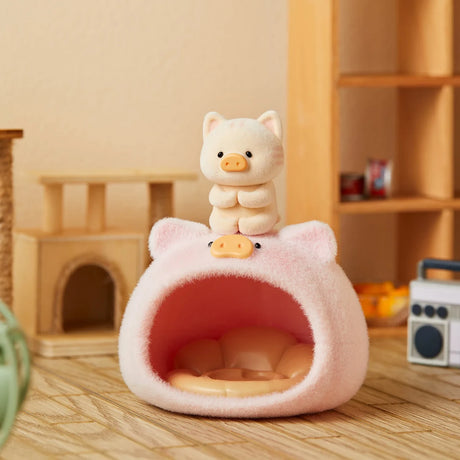 Small LuLu the Piggy figurine dressed as a white cat standing on a fluffy pink pig-shaped pet bed indoors