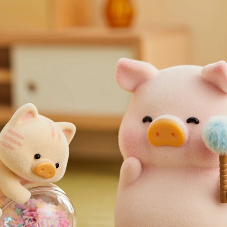 Soft pink LuLu the Piggy figurine holding a fluffy duster with a small cream cat figure beside a glass jar of colorful confetti