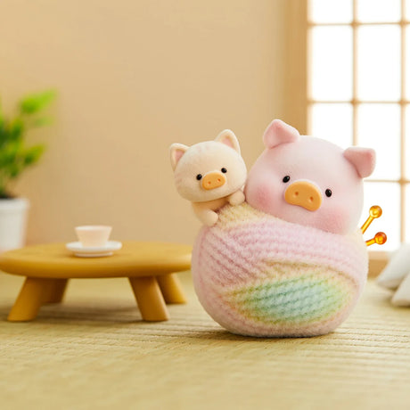 LuLu the Piggy figurine dressed as a cat with a smaller cat figure wrapped in pastel yarn in cozy room setting