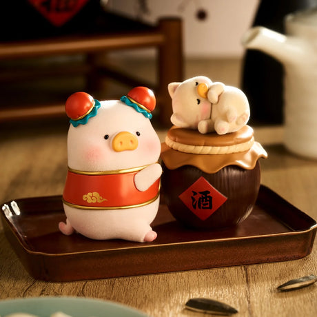 Pig figurine dressed in red with traditional hair buns standing next to a small jar topped with a sleeping cat figurine