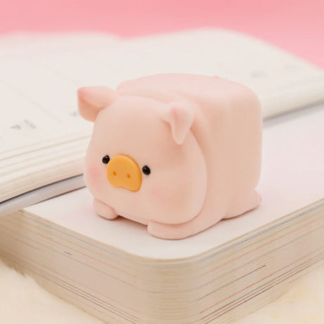 LuLu the Piggy Original Series 2 figure 8 with square shape and soft pink texture sitting on stacked books with pink backdrop