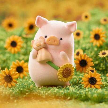 Soft pink LuLu the Piggy figure holding a small bear doll and wearing a sunflower crossbody bag in a field of sunflowers