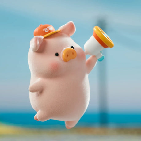 Pink LuLu the Piggy figure wearing orange cap and holding a megaphone with blurred beach background