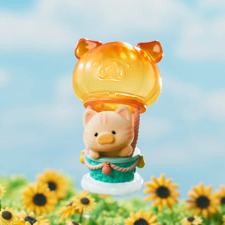 LuLu the Piggy figure riding in a translucent orange pig-shaped hot air balloon above a sunflower field