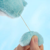 A hand pulls a string connecting two fluffy blue plush surfaces against a light blue background, demonstrating the LuLu The Piggy - Vibrating Shark Keychain in action.
