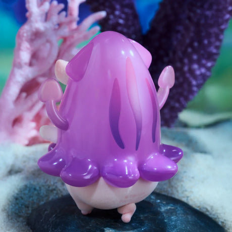 A small, pink and purple jellyfish-like toy from the LuLu The Piggy - Ocean Blind Box stands on a rock underwater with coral in the background—a perfect find for LuLu The Piggy fans and ocean-themed toy collectors.