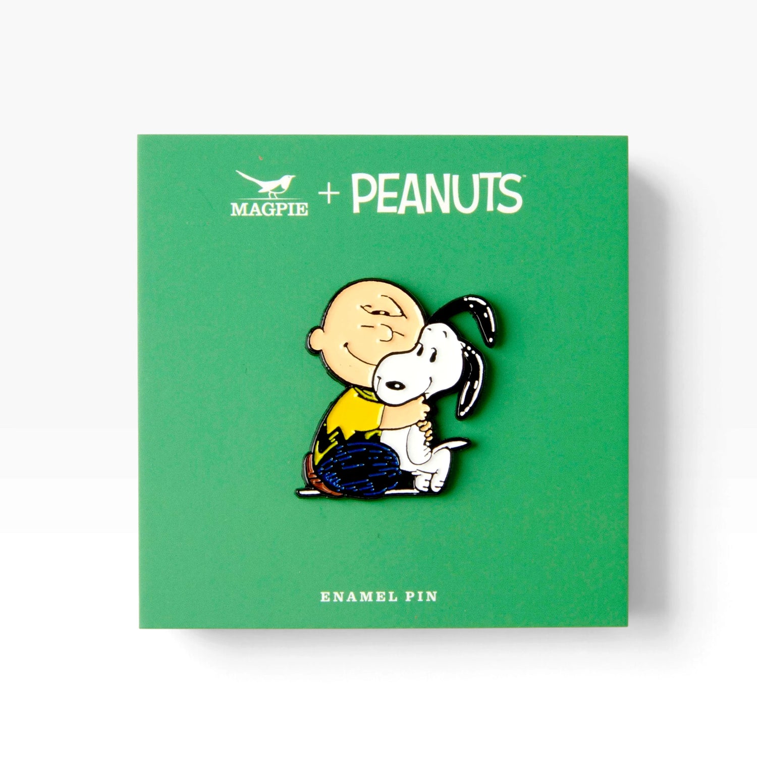 Enamel pin on green PEANUTS card with cartoon dog hugging a white puppy
