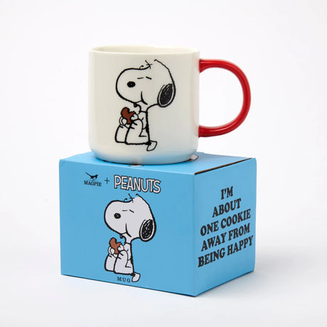 White ceramic Snoopy mug with red handle, Snoopy holding a cookie illustration.