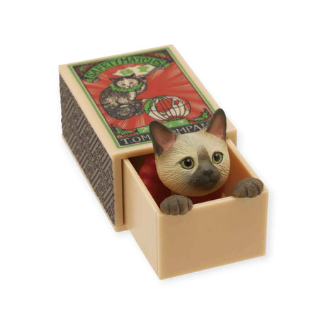 A charming miniature from the Kitan Club brand, known as the Cat in a Matchbox Blind Box, features a small cat peeking out of an open matchbox decorated with a nostalgic design of a kitty playing with a ball.