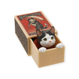 The Cat in a Matchbox Blind Box by Kitan Club is an adorable figurine featuring a black and white kitty peeking from a matchbox, crafted to emulate a classic safety match label.