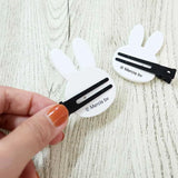 White bunny hair clips with black snap barrettes, held in a hand