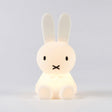 The Miffy Bunny Night Light, a 15cm lamp from the Miffy brand, features a glowing white design with long ears and minimal facial features. Made from BPA-free silicone for safety, it serves as a comforting nightlight against a plain backdrop.