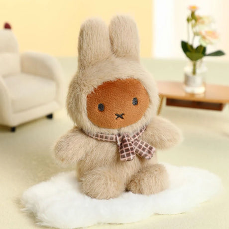 Plush Miffy keychain in cream fuzzy suit with checkered scarf sitting on soft white surface in cozy room setting