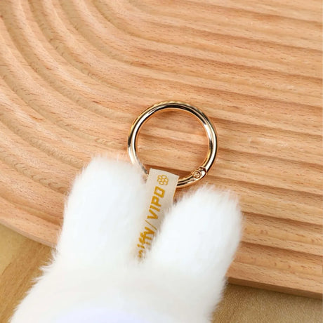 Close-up of white Miffy plush keychain with VIPO tag attached to gold keyring on wooden textured surface