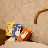 Three Miffy Soap - Berry Parfum packages, colorful and vegan-friendly, are arranged on a bathroom counter near a brass faucet, with a heart-shaped soap in the foreground.