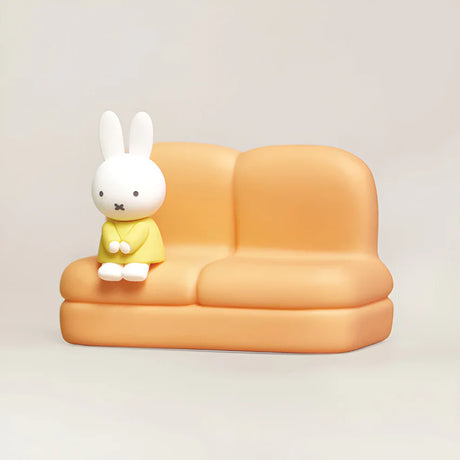 Mini Miffy figure in yellow outfit seated on smooth orange sofa stand against plain light background