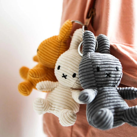 A pink bag is adorned with three Miffy Keychain Plushes - Corduroy 10cm, boasting eco-friendly designs in orange, white, and gray.