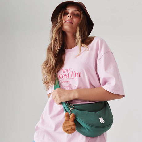 Model wearing green Miffy Crescent Crossbody Bag with brown plush charm and curved silhouette, promo image 3 in gallery