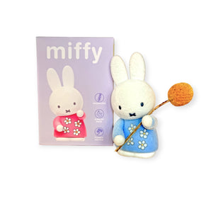 Plush white rabbit figure in a blue dress holding an orange pom-pom flower next to a lavender Miffy box