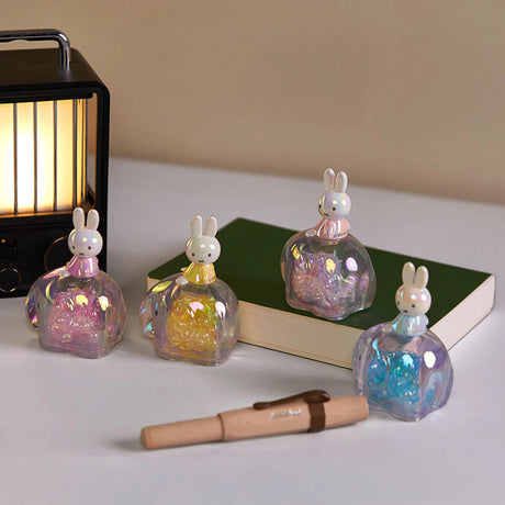 Four translucent elephant snowglobes with Miffy figures in pastel colors arranged with a lamp, book, and pen on white surface